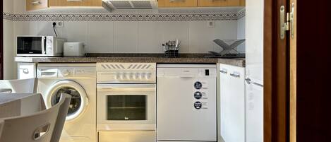 A compact kitchen with a washing machine, oven, and dishwasher.
