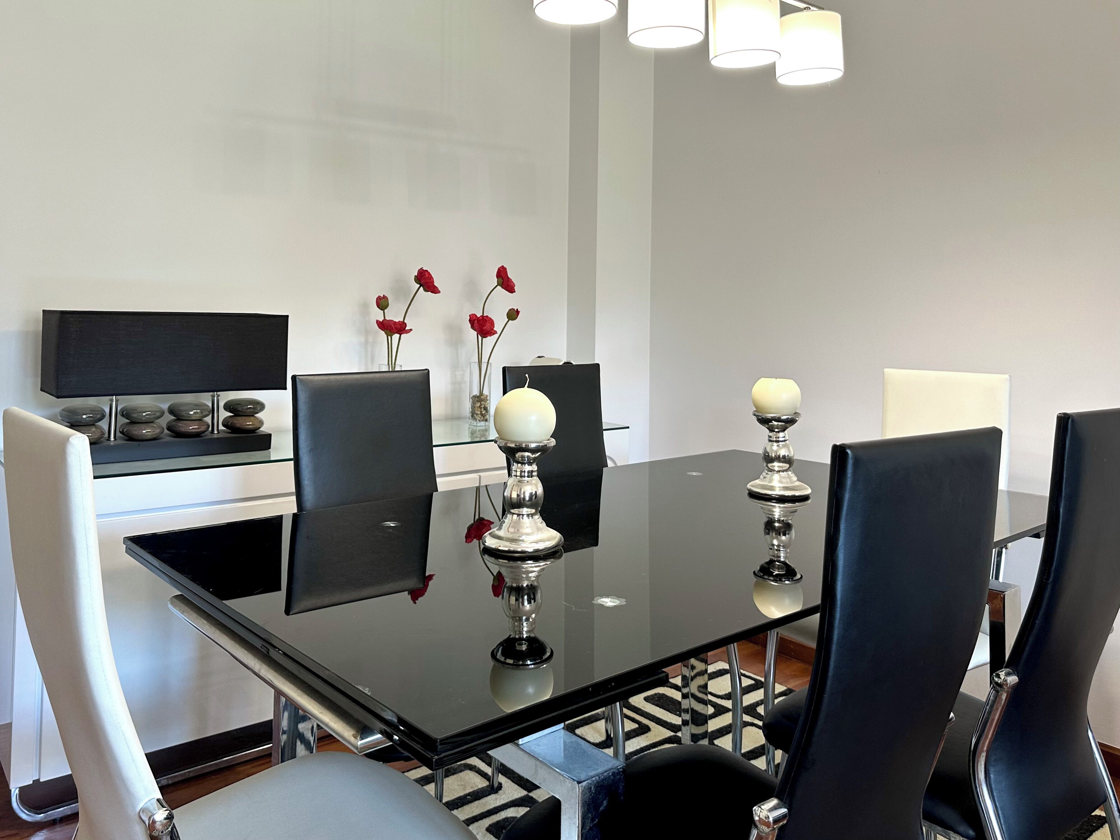 Een moderne vergaderzaal met een glazen tafel, zwarte stoelen, een zwarte televisie op een standaard en een vaas met rode bloemen.