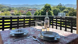 A table set for two with plates, cutlery, and a bottle on a balcony overlooking a scenic mountain view.