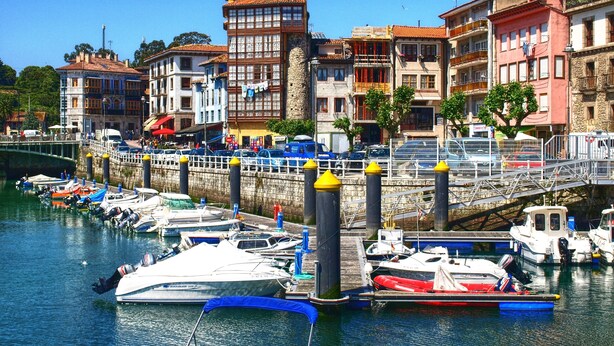 A marina with boats docked, a stone wall, and buildings with balconies.