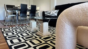 A modern living room with a black and white patterned rug, a glass coffee table, and a black sofa with a patterned pillow.