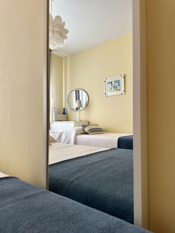 A hotel room with two beds, a bedside table with a lamp, a mirror, and a framed picture on the wall.