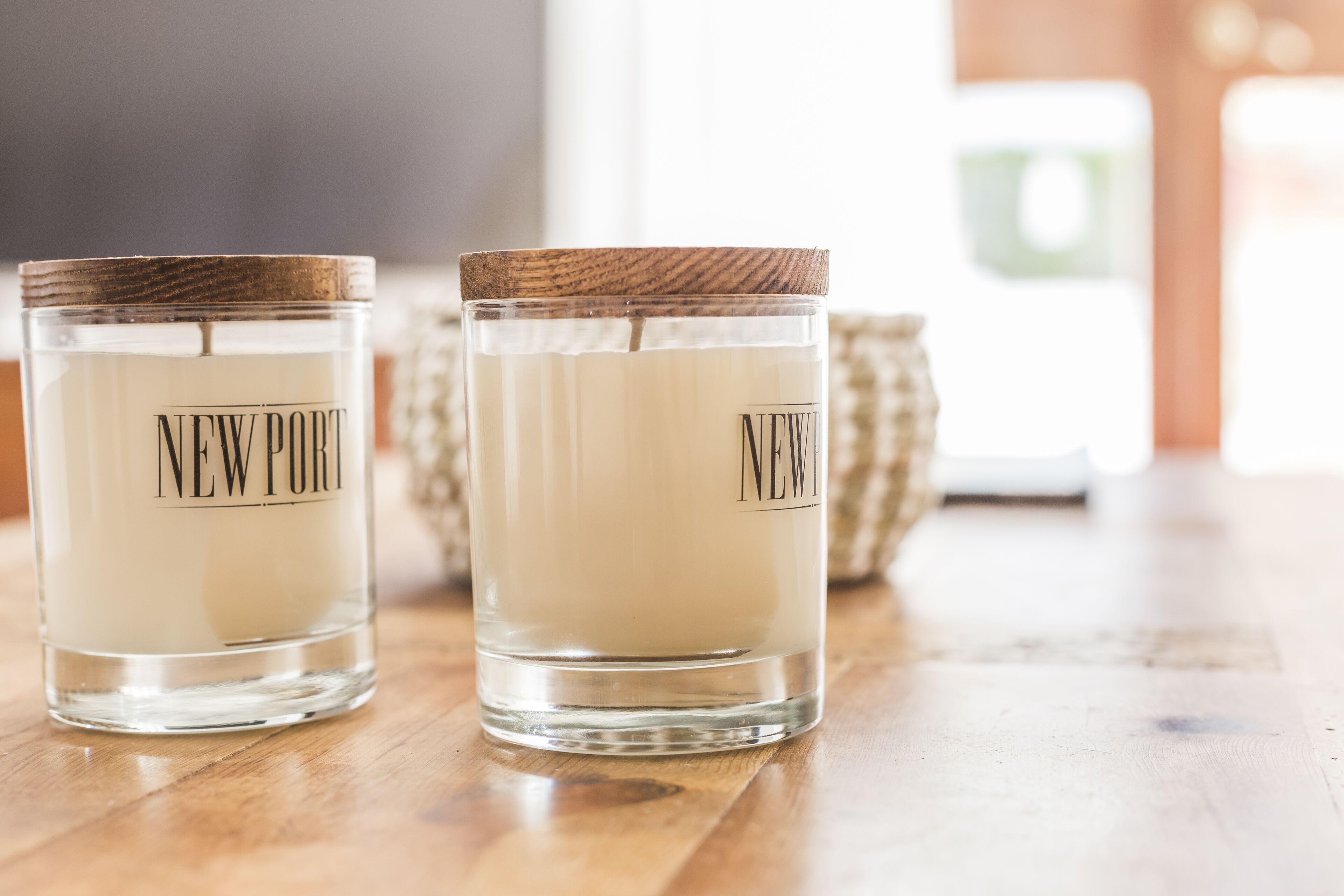 Two glass candle containers with wooden lids labeled "NEWPORT" on a wooden surface.