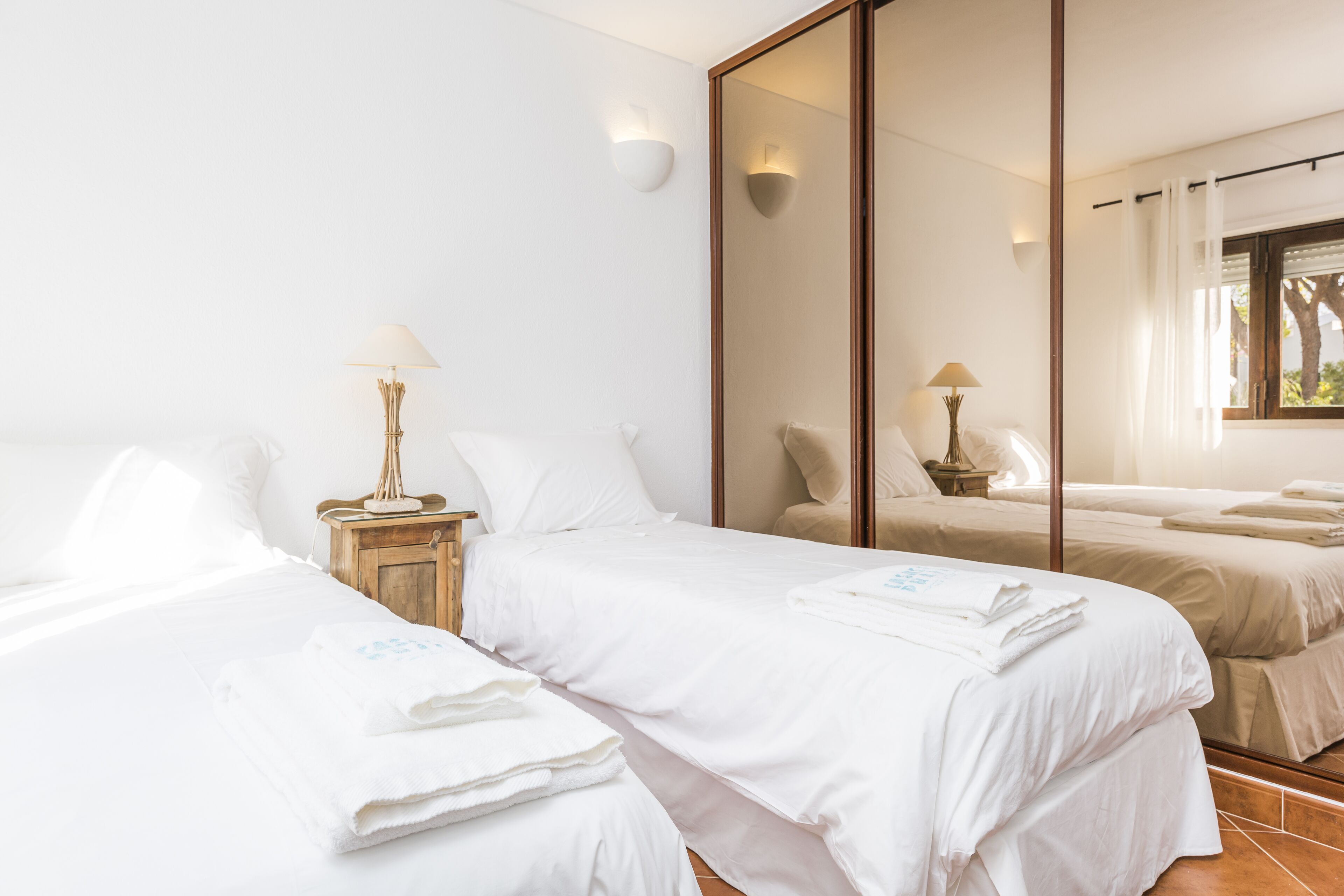 A hotel room with two beds, a large mirror, and a window with curtains.