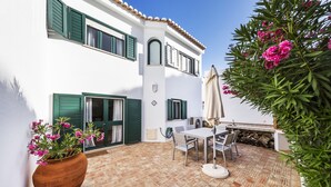 A patio with a table and chairs, a potted plant, and a building with green shutters. - CASAS DA PRAIA,   55 (Almancil)