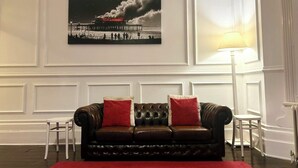 Ein Zimmer mit einem dunkelbraunen Ledersofa, zwei roten Kissen, einer weißen Lampe und einem gerahmten Bild an der Wand.