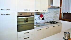 Eine moderne Küche mit weißen Schränken, einem eingebauten Backofen, einem Gasherd und einer Spüle aus Edelstahl.