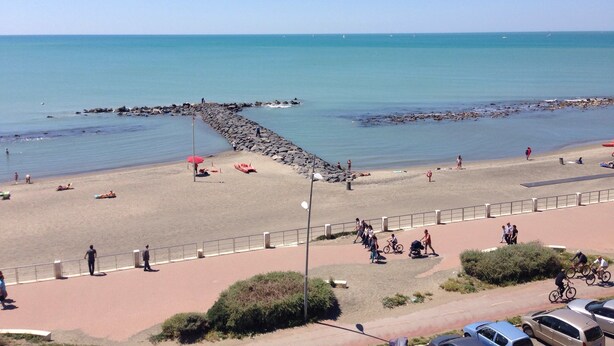 A beach with a rocky breakwater, a paved walkway, and parked cars.
