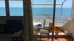 A balcony with a view of the sea, a table with shoes, and a chair.