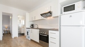 Una cocina moderna con gabinetes blancos, estufa de acero inoxidable, horno empotrado, microondas y cafetera.