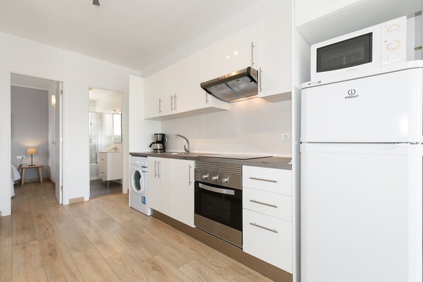 Una cocina moderna con gabinetes blancos, estufa de acero inoxidable, horno empotrado, microondas y cafetera.