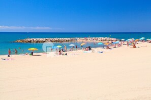 Una playa con gente tomando el sol y nadando, sombrillas y un rompeolas rocoso.
