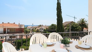Mesa en balcón con platos, cubiertos y vasos, con vistas a una zona residencial con casas y una grúa de construcción.