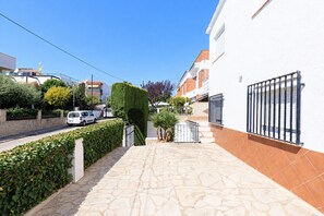 A paved walkway with a stone pattern, bordered by a hedge and a white building with a metal gate. - Lovely & Quiet Apartment near the Beach · UHC ACACIAS 120 (Cambrils)