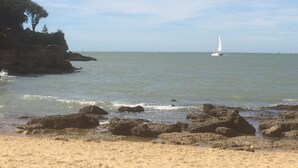 Une plage avec un rivage rocheux au premier plan et un voilier à l’horizon.