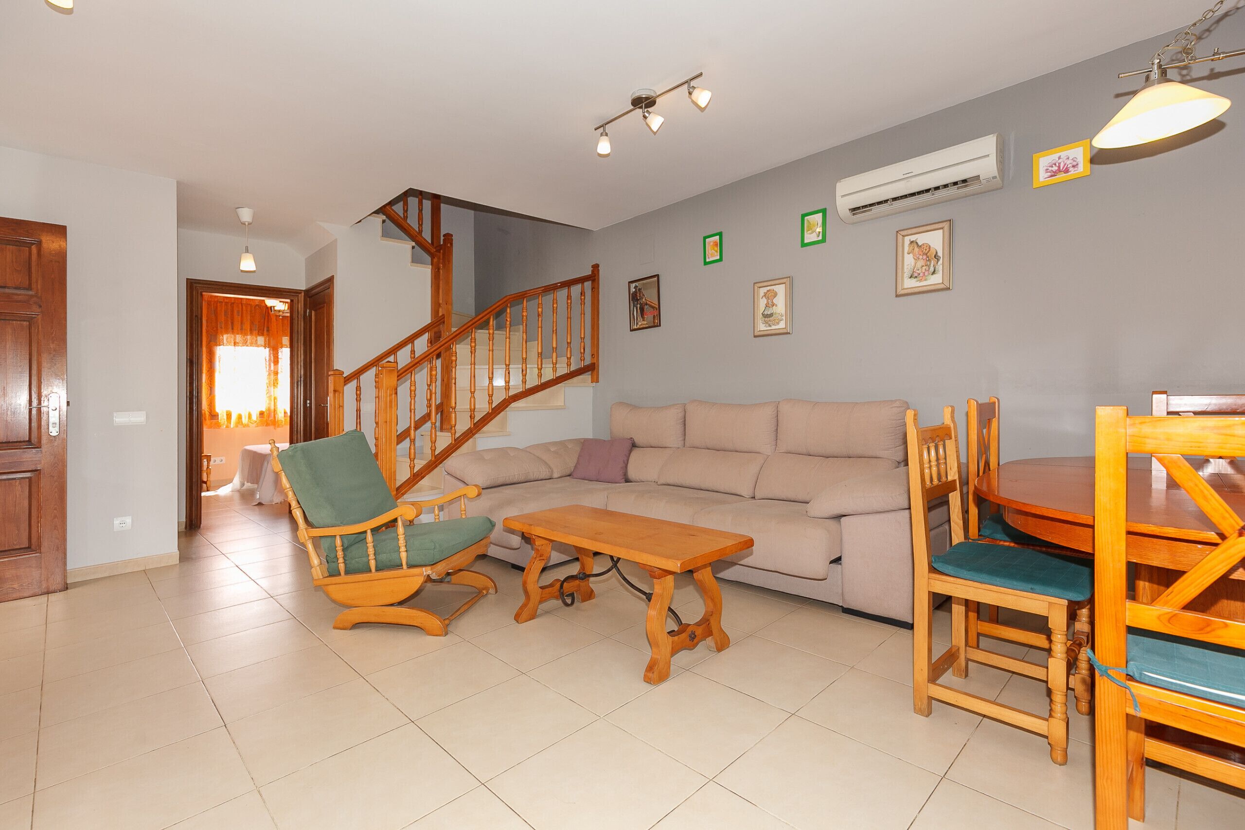 A living room with a wooden staircase, a sofa, a wooden coffee table, and a dining table with chairs.