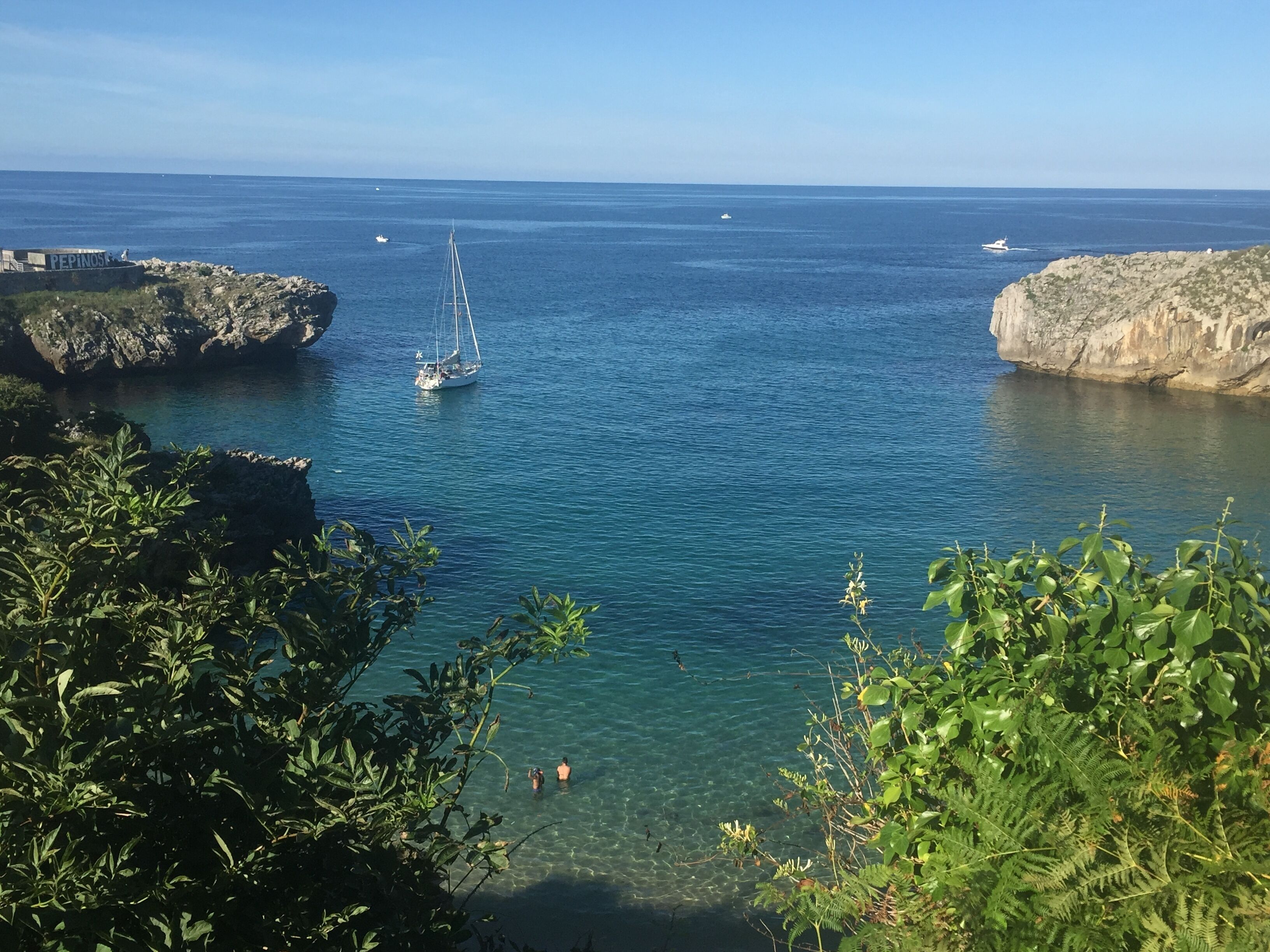 A coastal scene with clear blue water, rocky cliffs, and a sailboat.