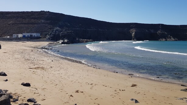 Une plage avec un petit bâtiment, un ciel dégagé et des falaises rocheuses.
