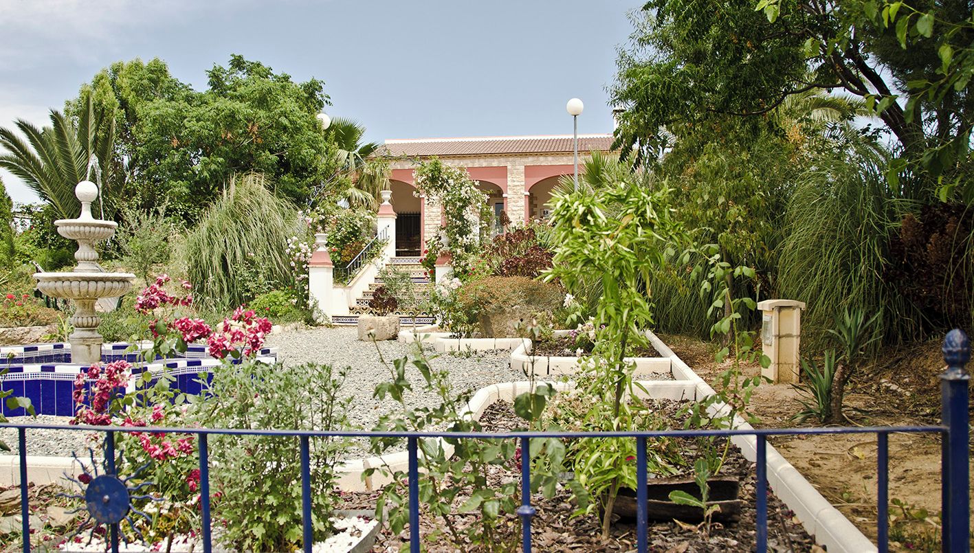 Una casa rural con jardín, una fuente y una escalera que conduce a la entrada.