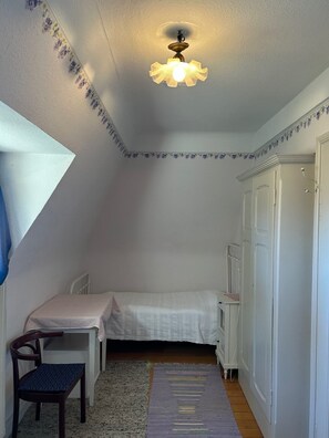 A small bedroom with a single bed, a chair, a desk, and a ceiling light fixture. - Beautiful apartment in a huge house in the Vosges (Hohrod)