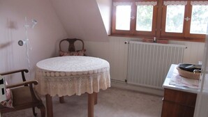 A cozy kitchen with a round table, a chair, a radiator, and a window with wooden shutters. - Lovingly furnished attic vacation apartment in Vosges house (up to 4 people maximum) (Hohrod)