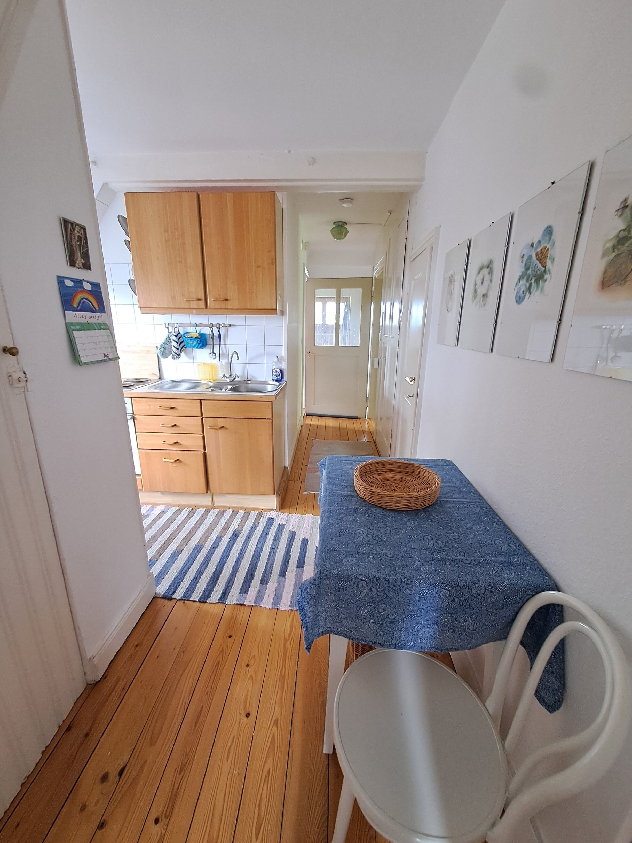 A narrow hallway leading to a kitchen with wooden cabinets, a sink, and a dining area with a table and chairs.