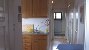 A narrow hallway with a kitchen area on the left, featuring wooden cabinets and a sink. A blue chair is placed in the hallway, and a striped rug is on the floor. - Lovingly furnished attic vacation apartment in Vosges house (up to 4 people maximum) (Hohrod)