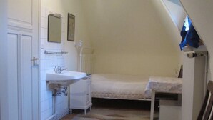 A small, narrow room with a single bed, a bedside table, a small desk, a white sink, and a mirror. - Lovingly furnished attic vacation apartment in Vosges house (up to 4 people maximum) (Hohrod)