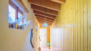 Un corridoio stretto con travi in legno al soffitto, pavimento piastrellato e una finestra con piante in vaso.