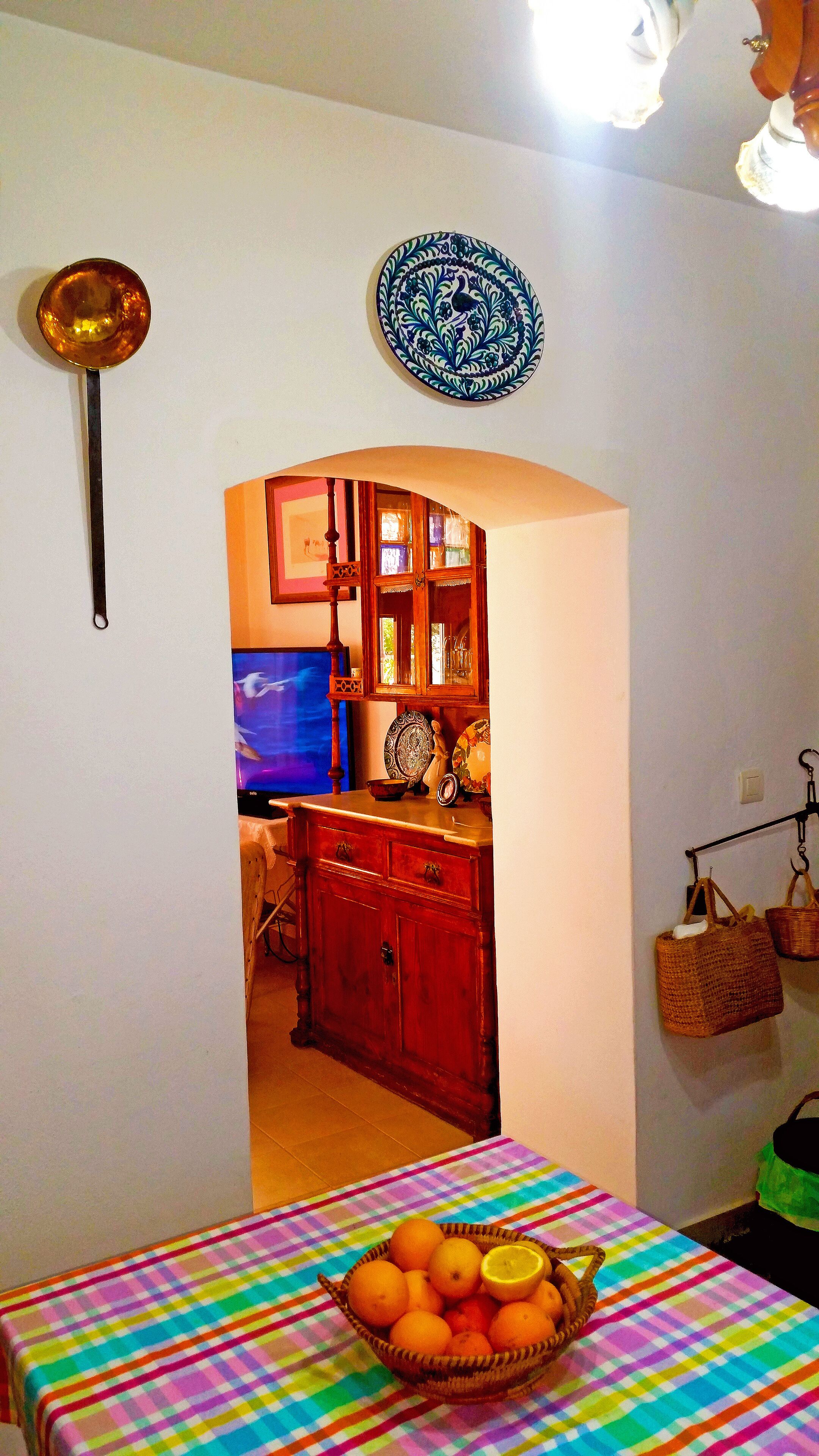 A dining area with a table set for two, a television in the background, and a kitchen visible through an archway.