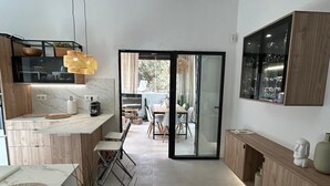 Een moderne keuken met een centraal eiland, een eethoek met tafel en stoelen, en een grote schuifdeur die leidt naar een buitenruimte.
