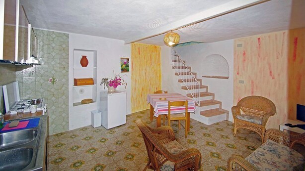 Ein kompakter Wohnbereich mit Küchenzeile, einem Esstisch mit Stühlen, einer Treppe und Korbmöbeln.