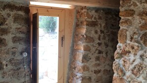A rustic stone interior with a wooden door leading to an outdoor area. - House Mmiriusa (Noto)