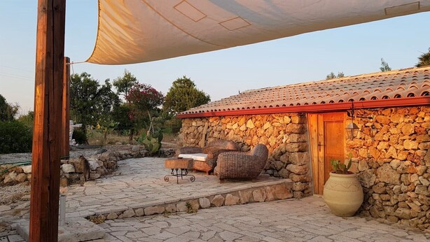 A stone building with a tiled roof, outdoor seating, and a large potted plant. - House Mmiriusa (Noto)