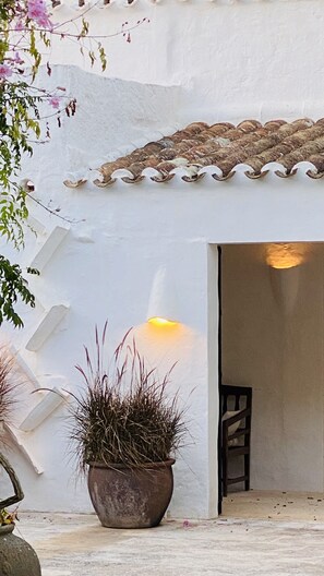 Un bâtiment blanc avec un toit recouvert de tuiles, un pot de fleurs devant et un escalier menant à l’étage supérieur.
