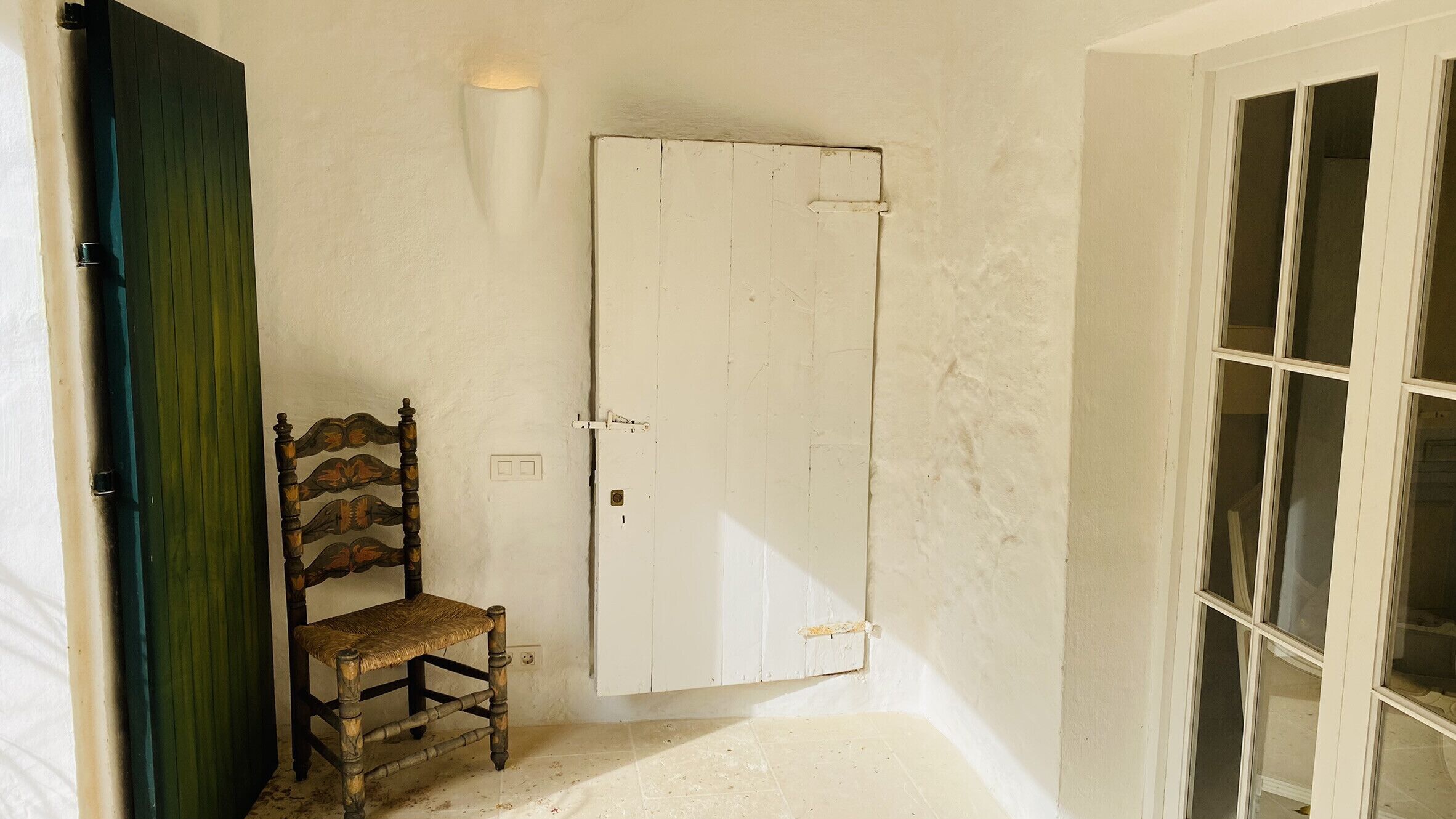 Una stanza con una sedia in legno, una porta bianca e una finestra a più vetri.