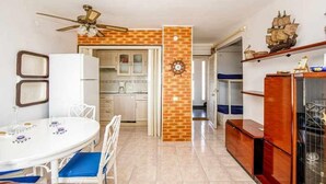 Une cuisine compacte avec un mur d’accent en briques, un coin repas avec une table blanche et des chaises bleues, et un meuble en bois agrémenté d’objets décoratifs.