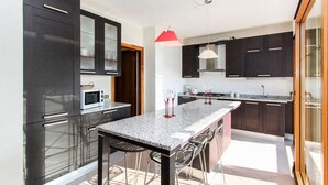 Une cuisine moderne avec des meubles de couleur sombre, un plan de travail en granit et un luminaire suspendu rouge.