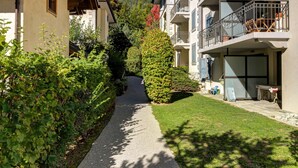 A pathway leading to a building with balconies, surrounded by greenery and mountains in the background. - Apartment Staddon - Alpes Agency - Central Chamonix - Sleeps 6 (Chamonix-Mont-Blanc)