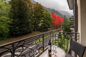 Un balcon avec vue sur une rivière, des arbres et des montagnes.