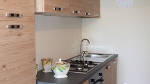 A kitchen with wooden cabinets, a gas stove, a sink, and a wall clock. - Casa Vacanza Etna - A OASI OF PEACE AND SERENITY (Linguaglossa)