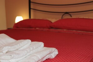 Een netjes opgemaakt bed met rode beddengoed en witte handdoeken gevouwen aan het voeteneind.