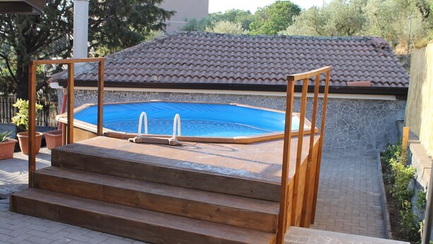 A swimming pool with wooden steps leading up to it, surrounded by a stone wall and potted plants. - Casa Vacanza Etna - A OASI OF PEACE AND SERENITY (Linguaglossa)