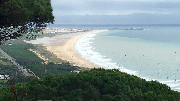 Un paysage côtier avec une plage, une route et un phare au loin.
