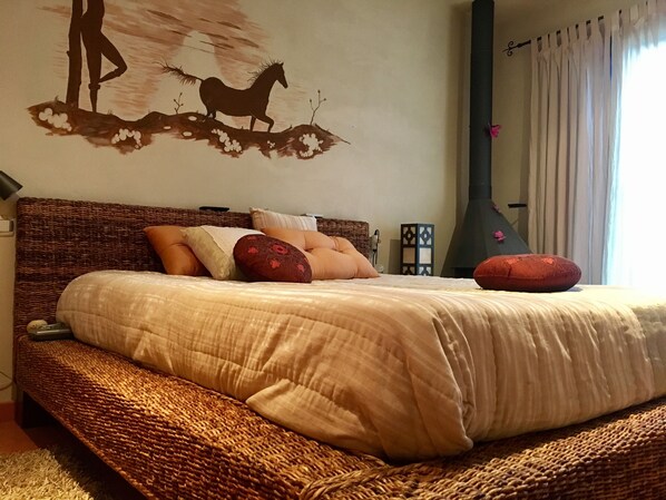 Een slaapkamer met een groot bed, een wanddecoratie, een open haard en een raam met gordijnen.