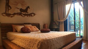 Un lit avec une tête de lit en osier, une grande fenêtre avec des rideaux et une cheminée fixée au mur.