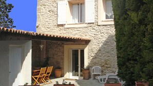 A stone building with a tiled roof, a door, and windows. There are potted plants and outdoor furniture. - Vineyard cottage classified 4* with large pool between Carcassonne and Narbonne (Ferrals-Les-Corbières)