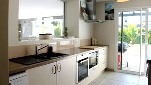 A modern kitchen with a large window, a built-in oven, and a sliding glass door leading to a patio. - Villa Celtitude - Villas of Sands  (Plurien)