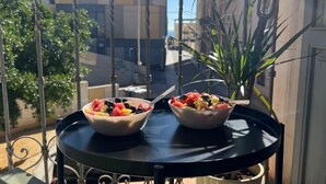 Un balcon avec deux corbeilles de fruits posées sur une table, entouré de plantes en pot et d’une rambarde en métal.