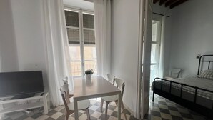 Une pièce avec un sol à carreaux, un lit, une télévision, une table avec des chaises et une fenêtre avec des rideaux.
